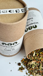 Two cardboard containers of 'Woman Blooms' cleanse tea with visible tea leaves on a white background.